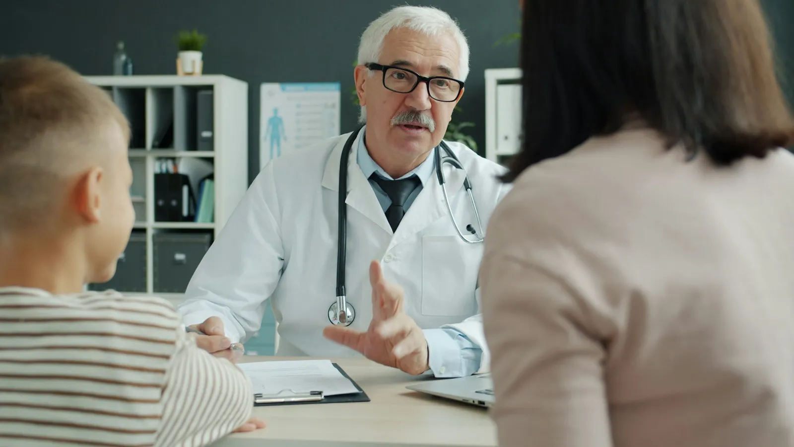 Médico a conversar com mãe e filho no consultório
